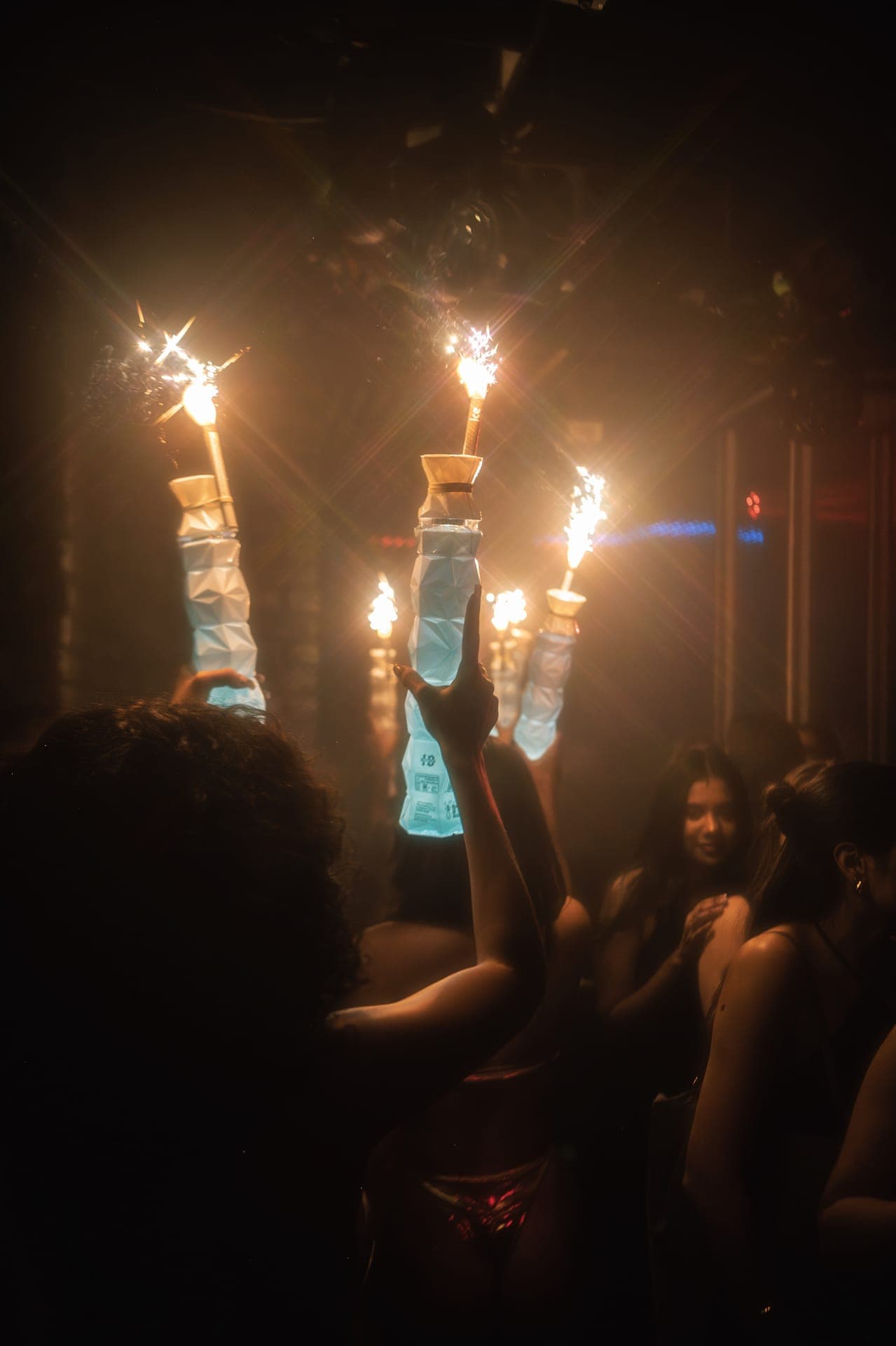 Guests in a dimly lit club holding up bottles topped with lit sparklers
